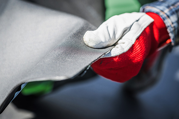 A roofer holds a sheet of EPDM roofing in a gloved hand.