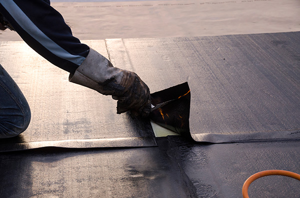 A person's arm and hand smoothing bitumen roofing material onto a flat roof.