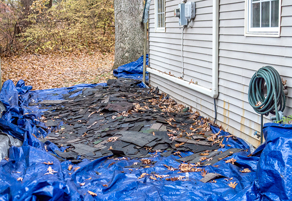 A messy pile of discarded shingles, grass protected by a tarp