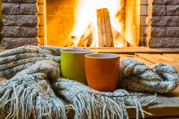 Two mugs and a blanket in front of a roaring fireplace