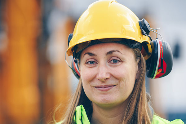 Smiling woman roofer in a hardhat and safety earphones