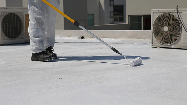 A roofer applies a white roof coating to a flat roof.