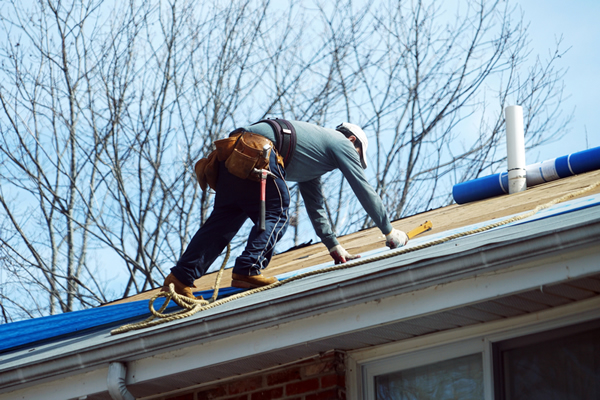 Contractor in hard hat and tool belt repairing a roof