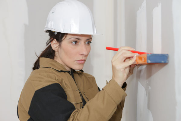 Contractor marking drywall with a pencil and level