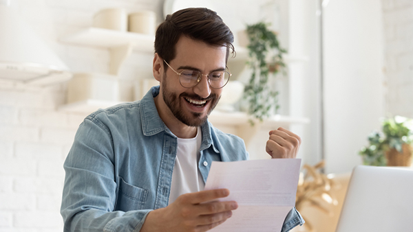Man wearing glasses and smiling while reading a piece of paper