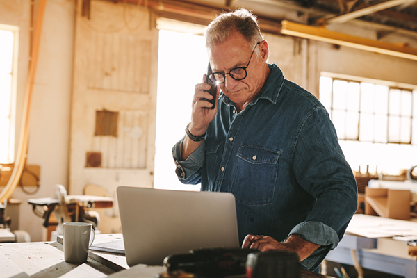 Senior contractor with glasses using a laptop and cell phone