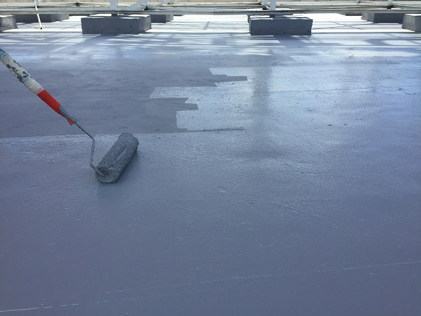 A roofing professional applying a coating to a flat roof with a roller