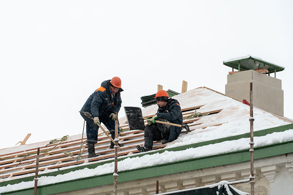 Two roofers wearing safety equipment on a snowy roof.