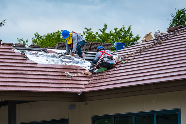 Two roofers in harnesses fixing a portion of a tile roof