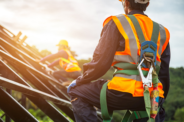 Two construction workers using safety harnesses while working on a roof frame