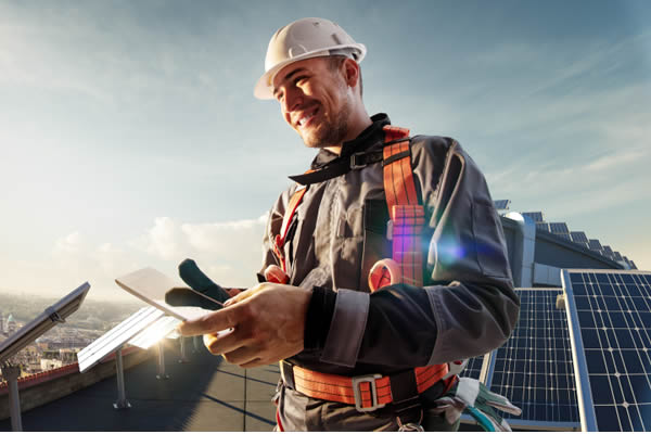 Smiling roofer using tablet on a roof with solar panels