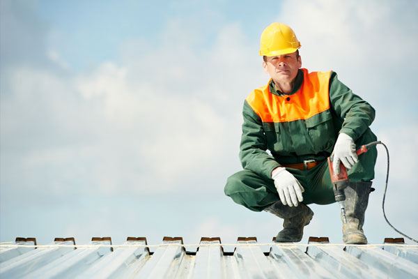 A roofer squats on a roof.